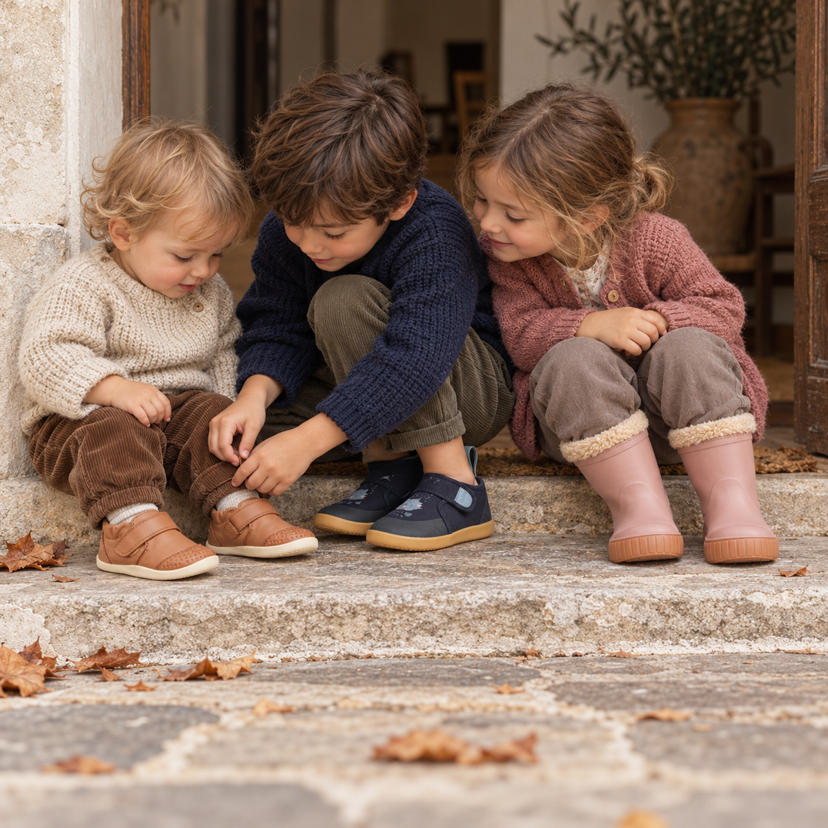 Tre bambini con scarpe primi passi color caramello, scarpe blu e stivali rosa della collezione inverno 2026